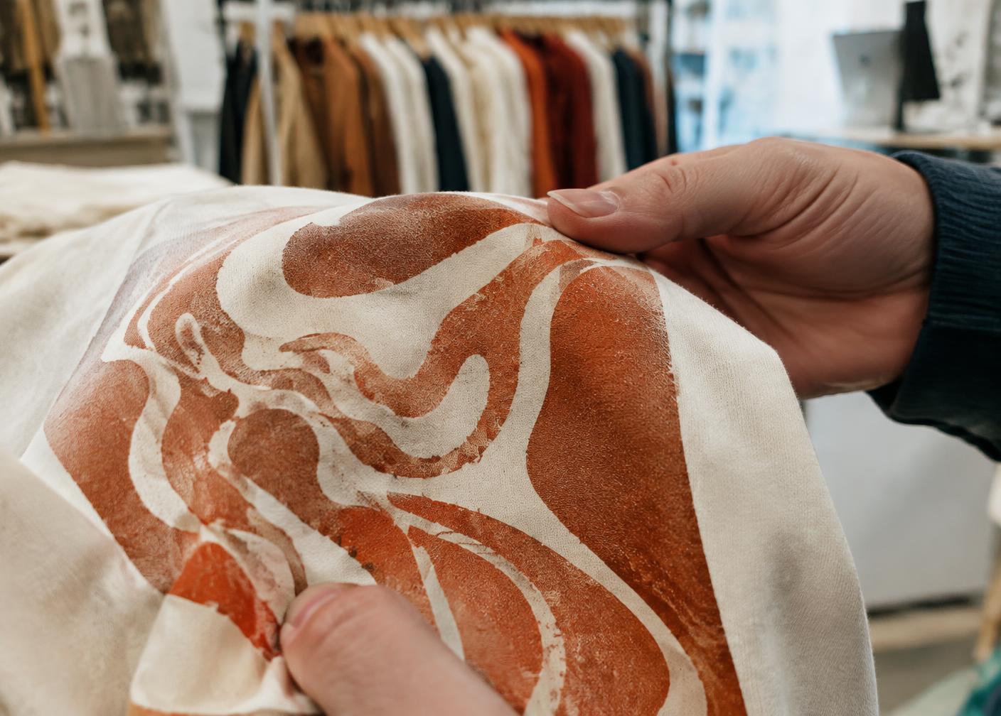 Hands inspecting a terracotta print on a cream heavyweight tee
